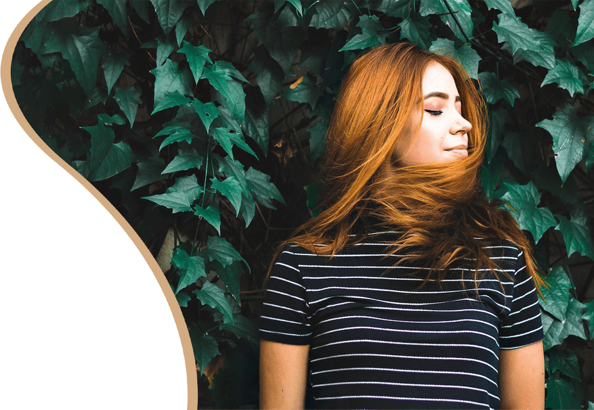 A woman with red hair standing in front of a tree.